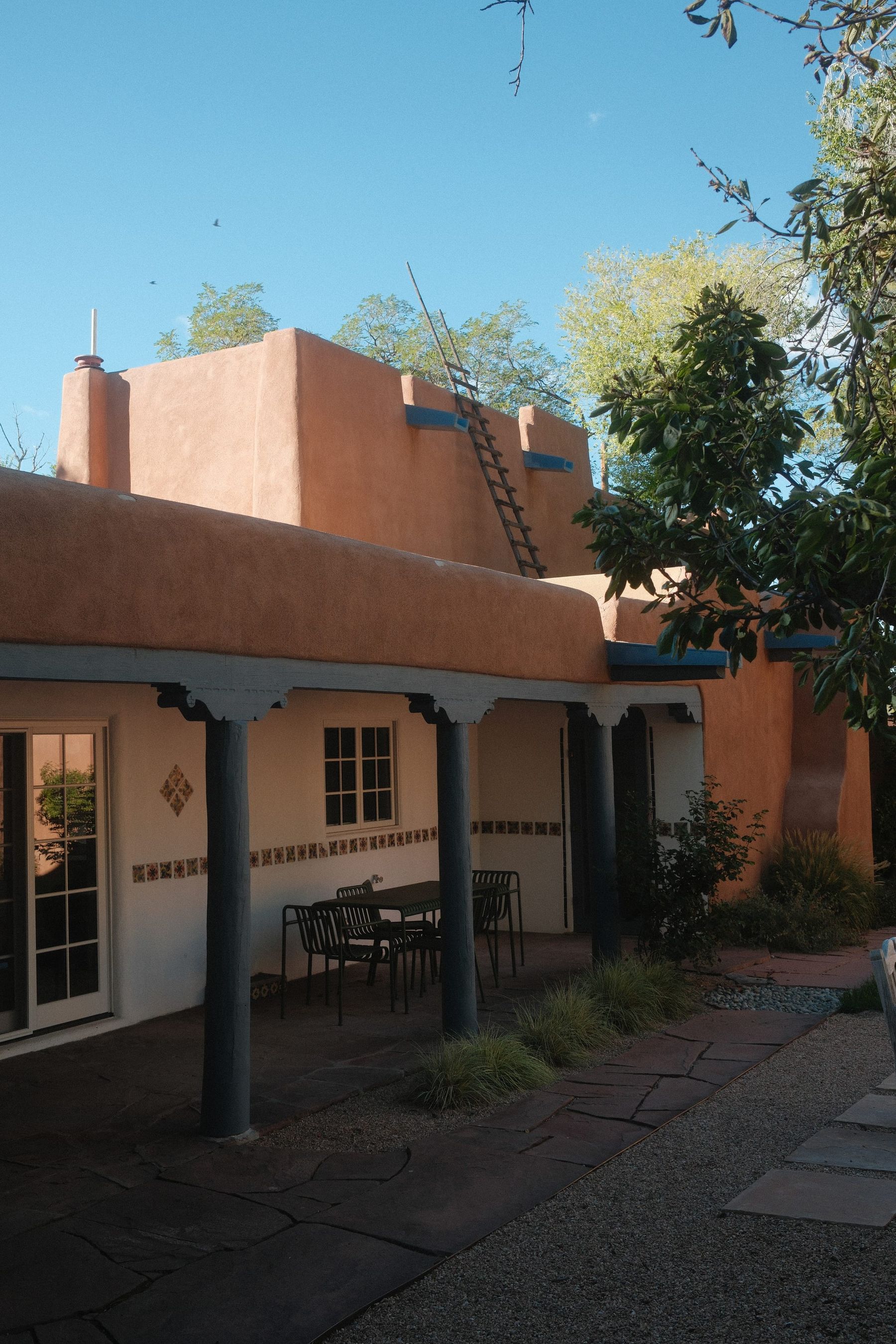 An adobe house with a deep portal on blue posts, under a clear sky
