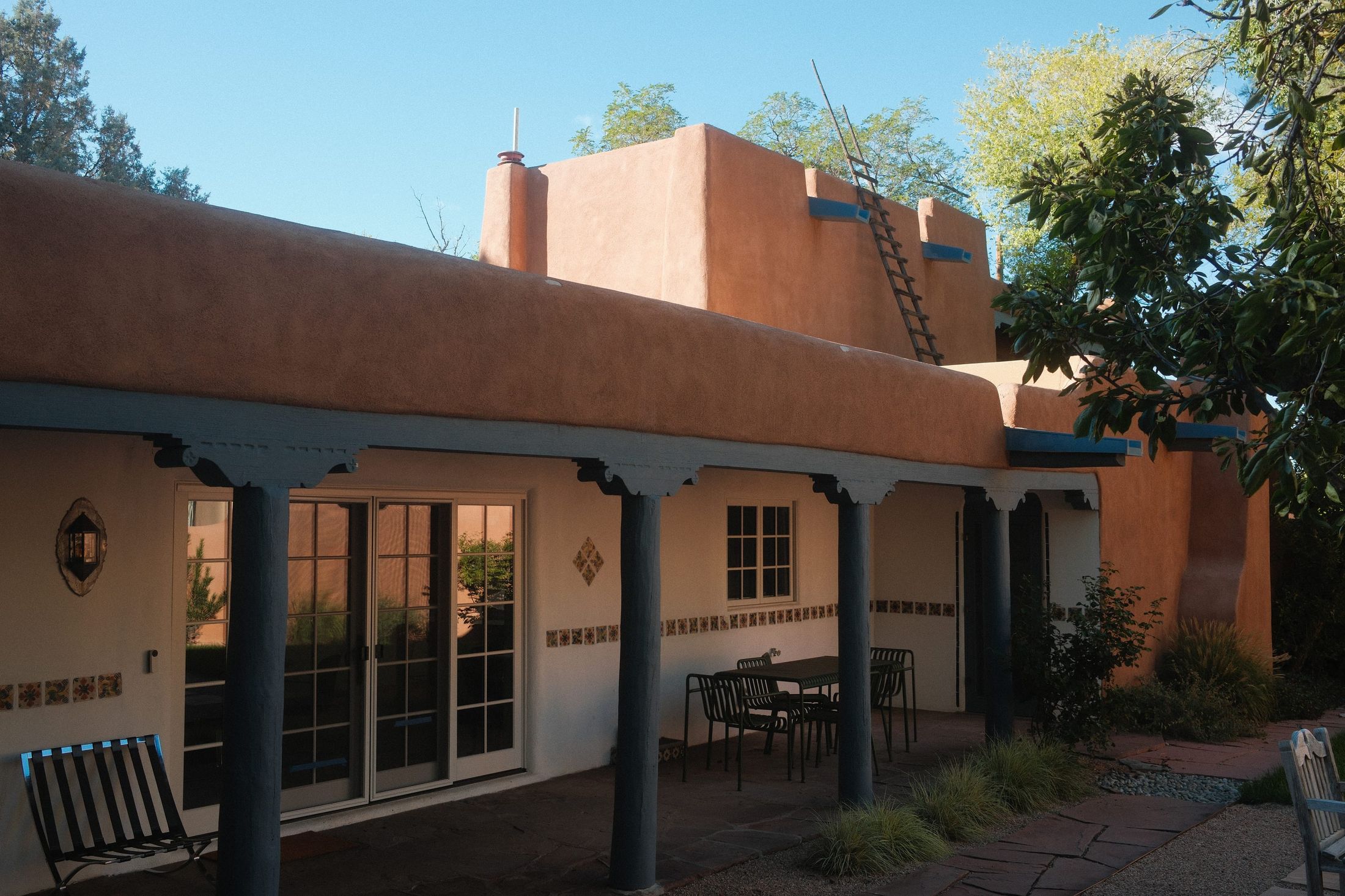An adobe house with a deep portal on blue posts, under a clear sky
